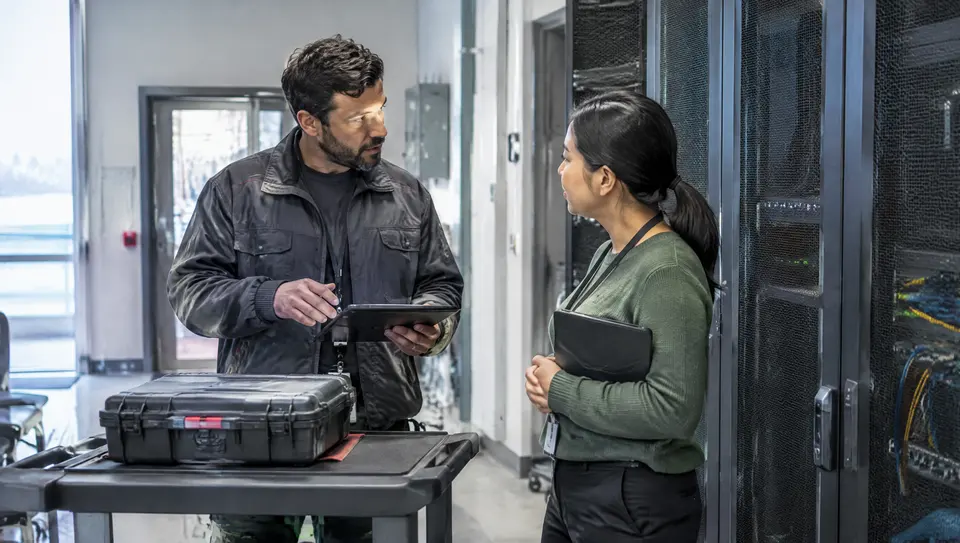 Field and operations colleagues coordinate a planned handover in a technical room with closed tools.